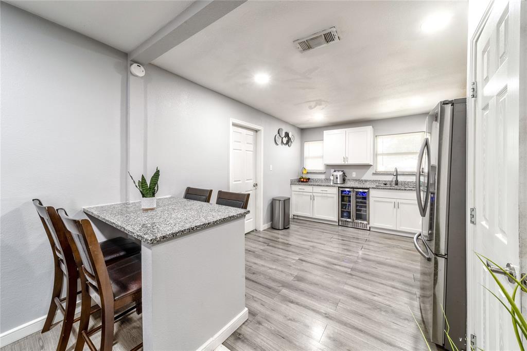 Kitchen with freestanding refrigerator, light stone counters, a breakfast bar, white cabinets, and wine cooler