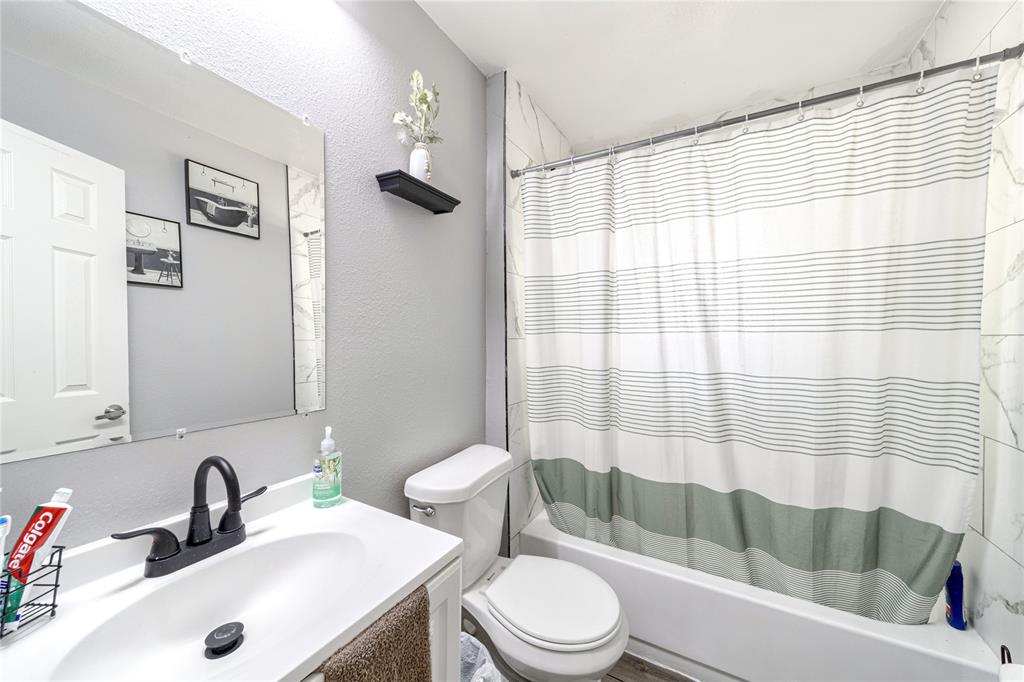 Full bath featuring vanity, a textured wall, and shower / bathtub combination with curtain