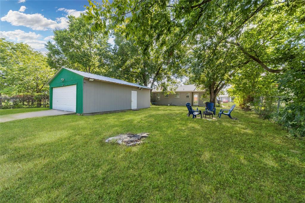 View of yard featuring an outbuilding, a detached garage, an outdoor fire pit, and view of wooded area