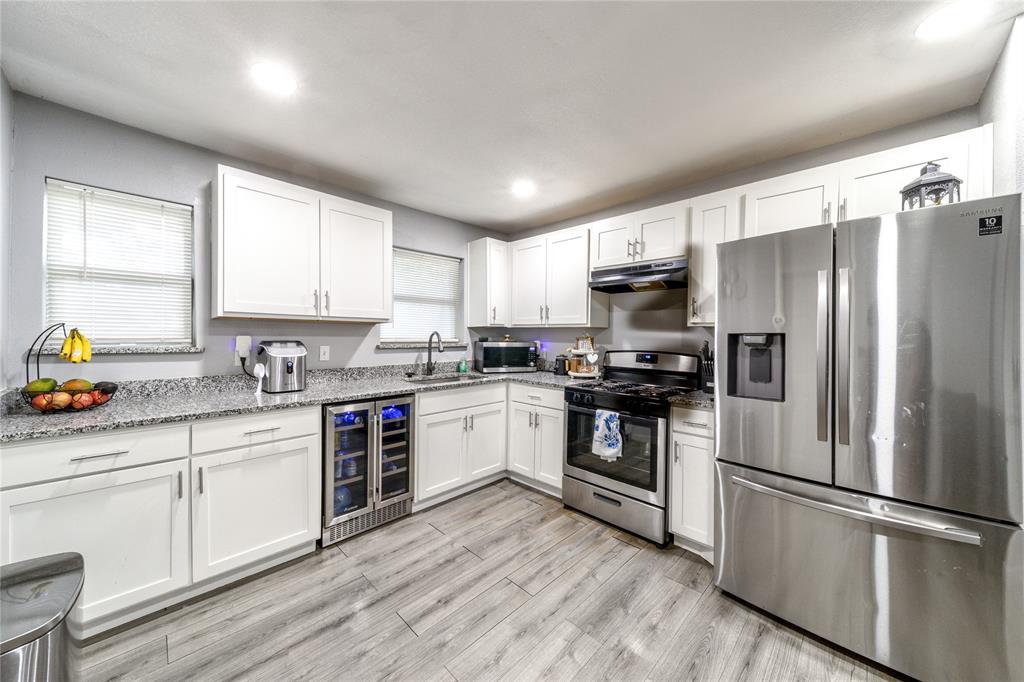 Kitchen featuring stainless steel appliances, wine cooler, white cabinets, recessed lighting, and light stone countertops