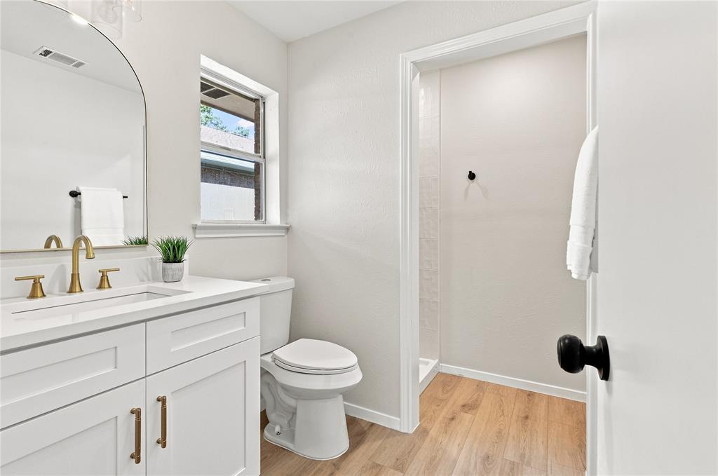 White vanity with gold-finish fixtures and hardware, rectangular undermount sink, and a framed arched mirror