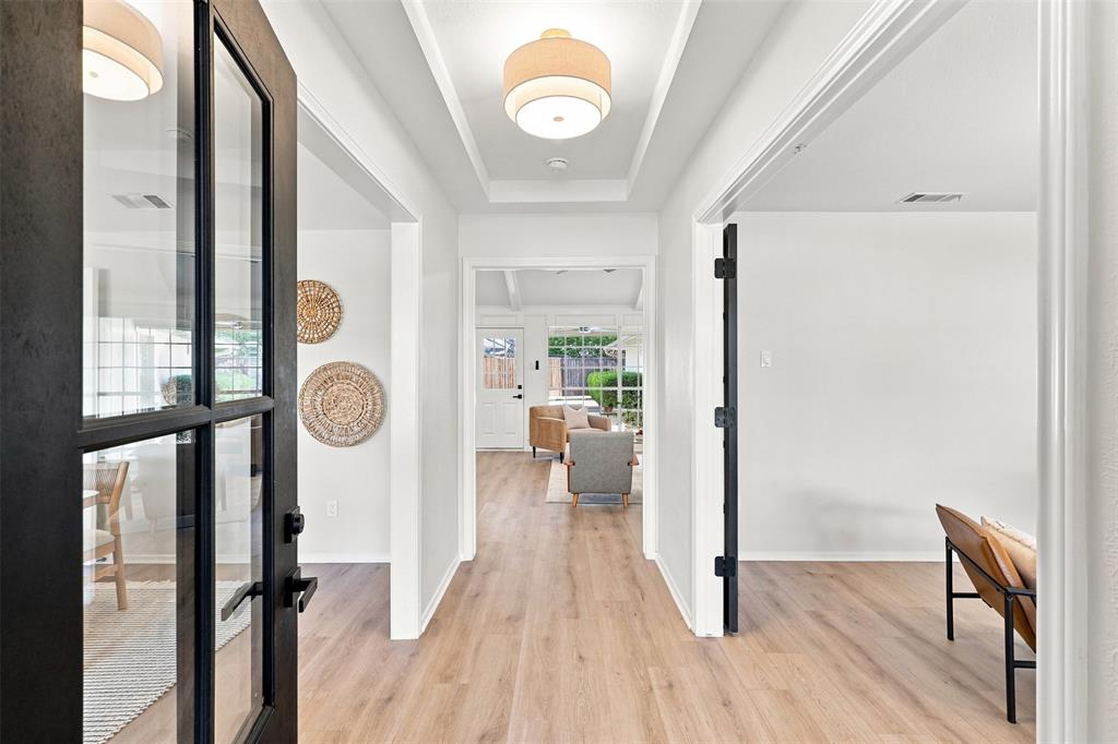 Light wood-finish flooring extending throughout, coffered ceiling, recessed lighting, and a black-framed glass panel door