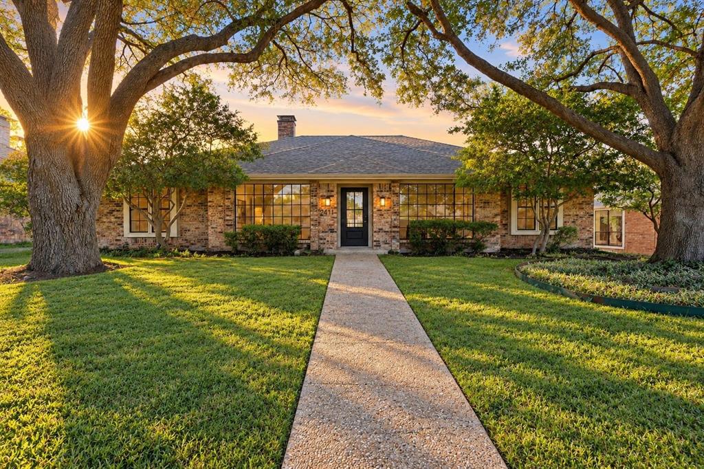 Brick exterior with a dark-paneled front door, an extensive front lawn, mature trees, and a concrete walkway