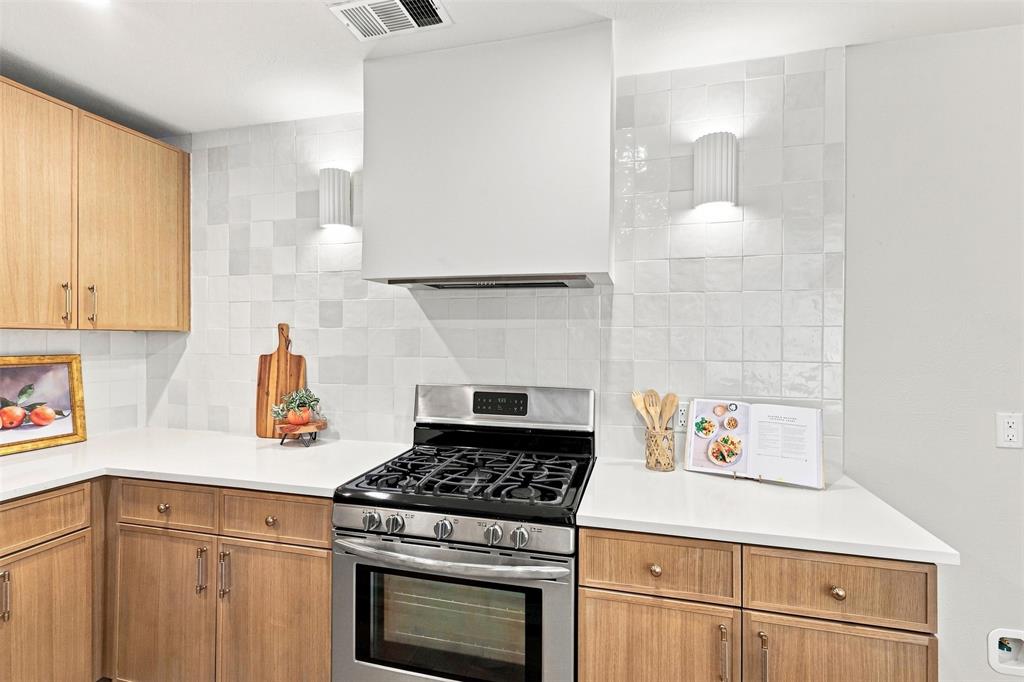 Modern kitchen featuring warm wood-finish cabinetry, white subway tile backsplash, stainless steel gas range with convection oven, and white quartz countertops with ample workspace and storage throughout