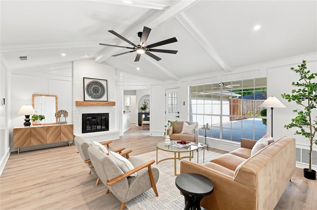 Vaulted ceiling with exposed beams, brick fireplace with wood mantel, large pane windows, wood-finish flooring, and recessed lighting