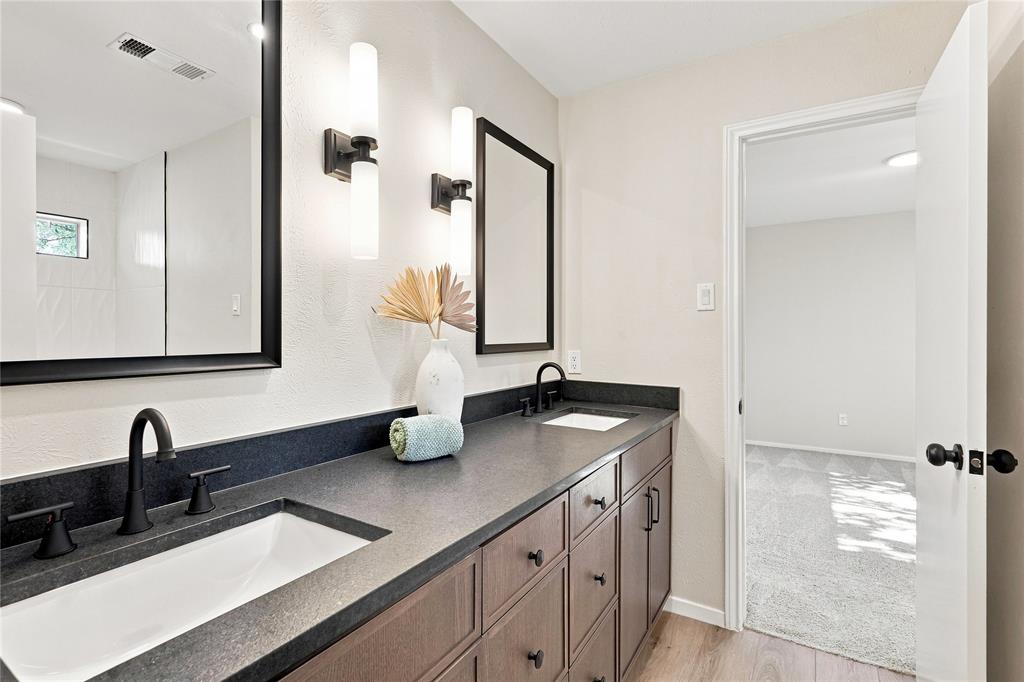 Dual sink vanity with dark wood-finish cabinetry, black countertops, and matte black fixtures
