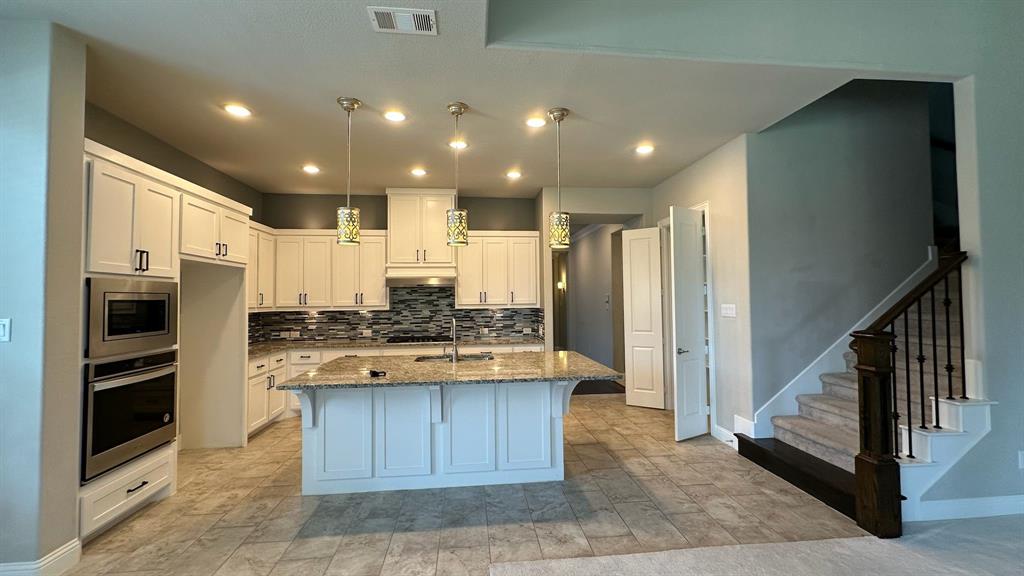 Gourmet kitchen featuring a large island with a stone countertop, white cabinetry with dark hardware, stainless steel appliances, and a mosaic tile backsplash