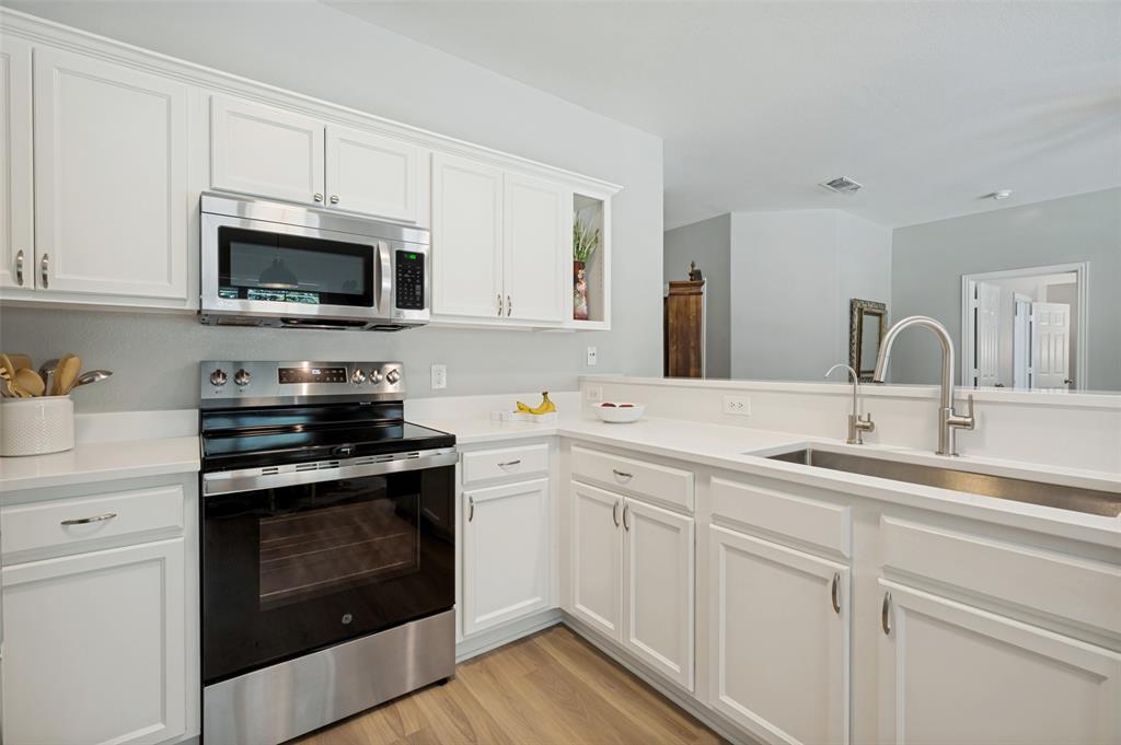 Contemporary kitchen featuring white cabinetry with brushed nickel hardware, stainless steel appliances including a built-in wall oven and microwave, quartz countertops, and a spacious island with an undermount sink and chrome pull-down faucet