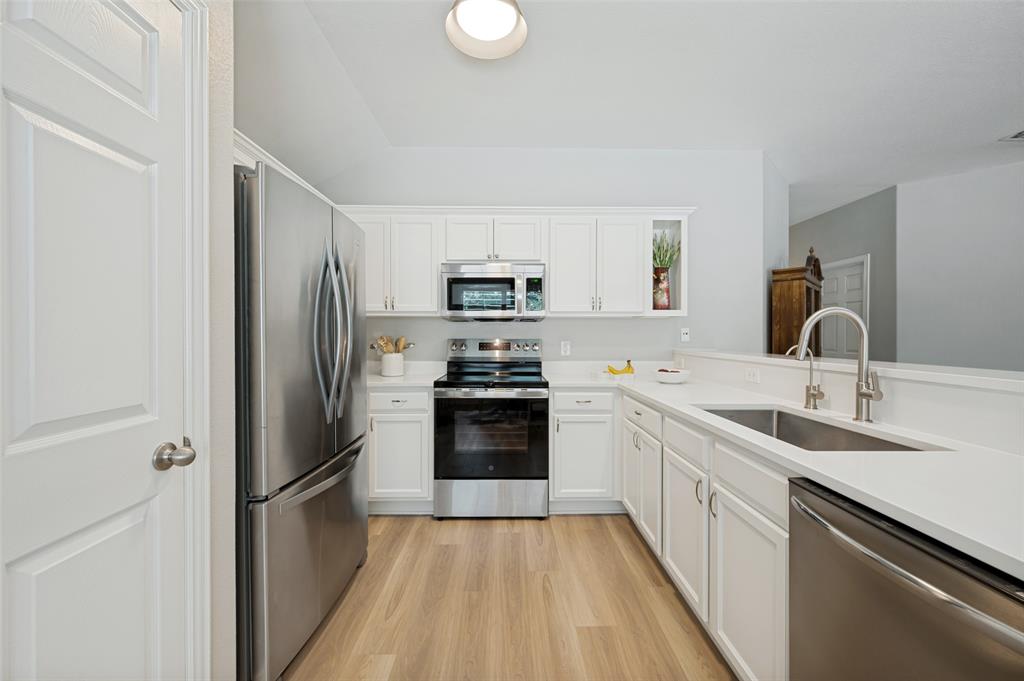 Kitchen featuring white cabinetry, stainless steel appliances, light-toned countertops, a dual basin sink, and wood-finish flooring