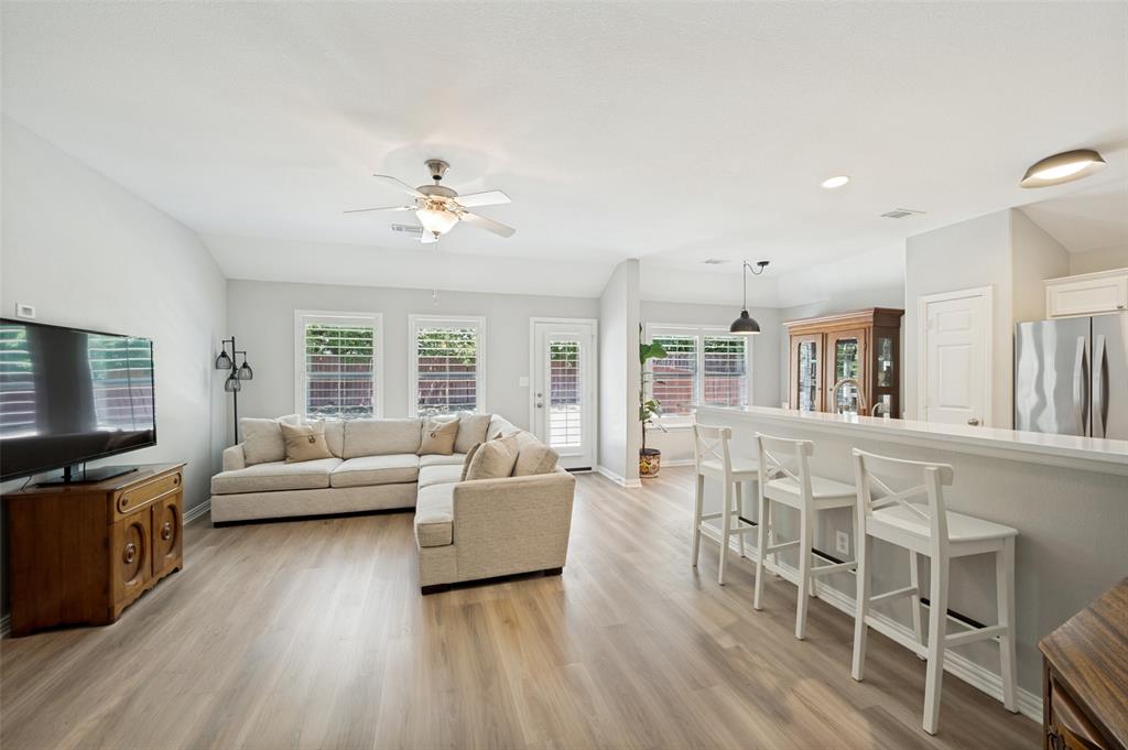 Expansive room featuring wood-finish flooring, a ceiling fan with light fixture, and multiple windows with plantation shutters