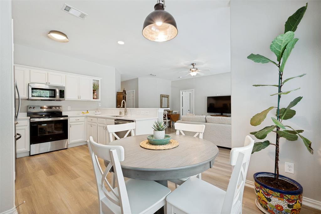 Kitchen featuring white cabinetry, stainless steel appliances, solid surface countertops, wood-finish flooring, and a breakfast bar