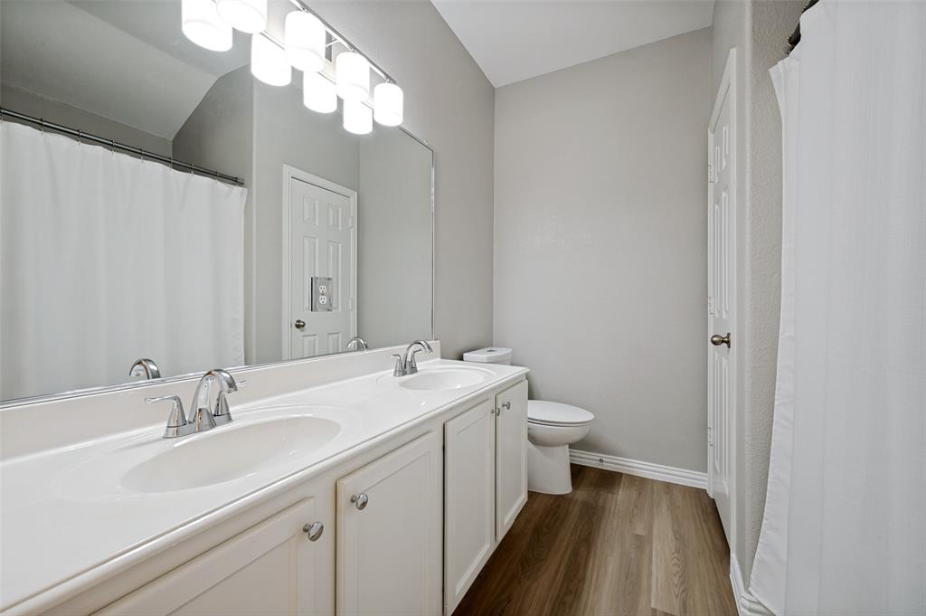 Double vanity with chrome fixtures and integrated sinks, wood-finish flooring, and a large wall-mounted mirror