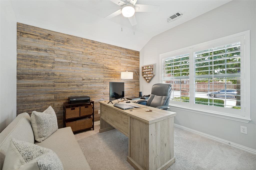 Guest bedroom with a ceiling fan, accent wall with wood paneling, large windows with plantation shutters, and carpeted flooring