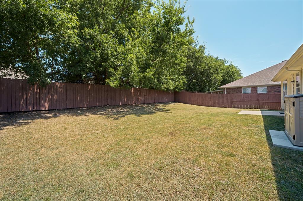 Expansive backyard with a full privacy fence, mature trees, and a concrete patio