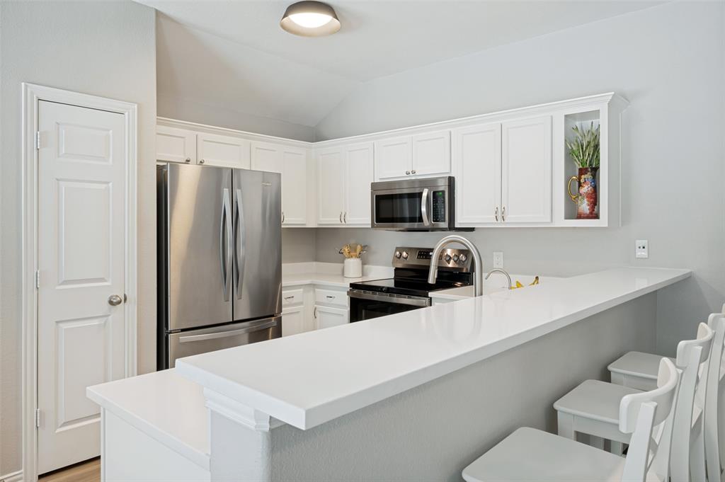 White shaker cabinetry, stainless steel appliances, white countertops, built-in microwave, and a breakfast bar