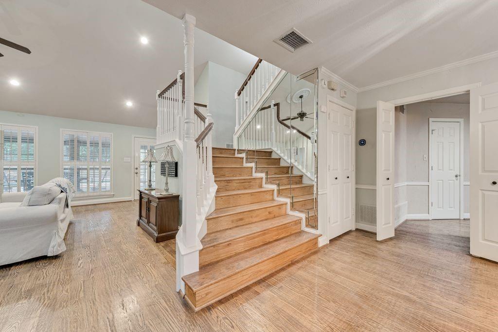 Hardwood flooring throughout, a grand staircase with wood newel posts and white balusters, recessed lighting, and multiple windows with plantation shutters