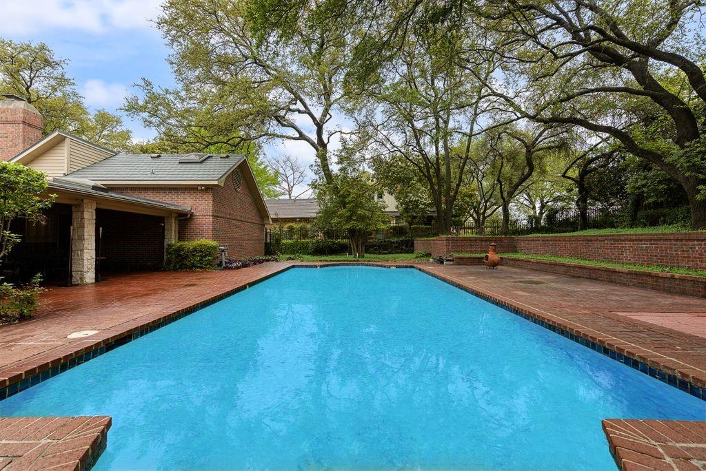 Elongated swimming pool surrounded by brick coping and a spacious brick patio Elongated swimming pool surrounded by brick coping and a spacious brick patio