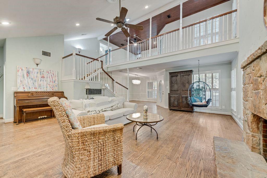High ceilings with exposed wood beams, wood-finish flooring, two-story stone fireplace, white baluster staircase, and abundant natural light