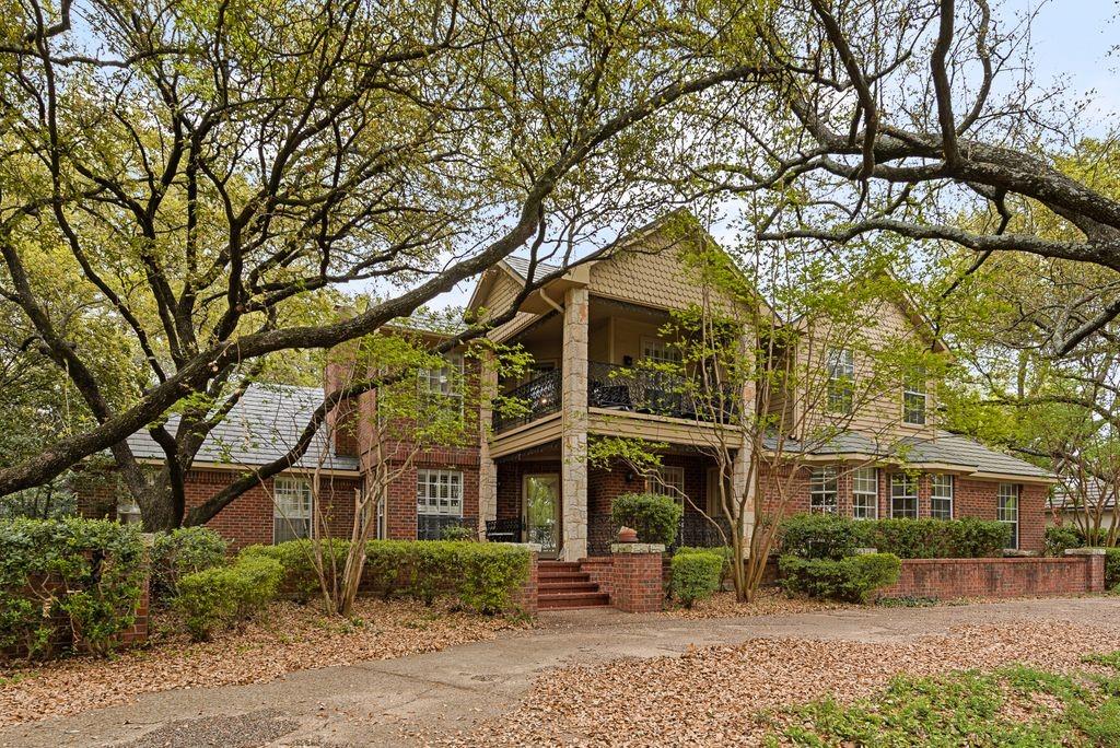 Brick exterior with a stone column porch, an upper-level balcony, dormer windows, and a multi-level roofline
