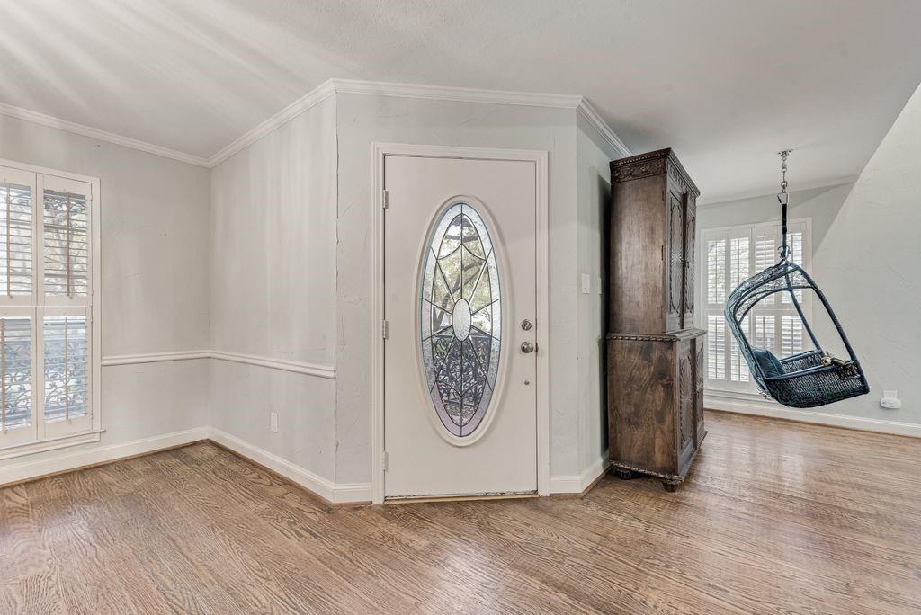 Entryway featuring wood-finish flooring, a front door with an oval stained-glass insert, and white plantation shutters