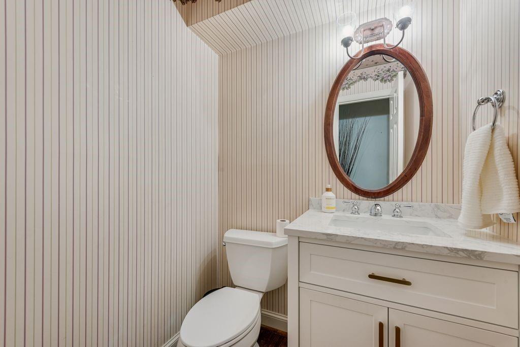 White vanity with a stone countertop, an oval wood-framed mirror, and a chrome towel ring