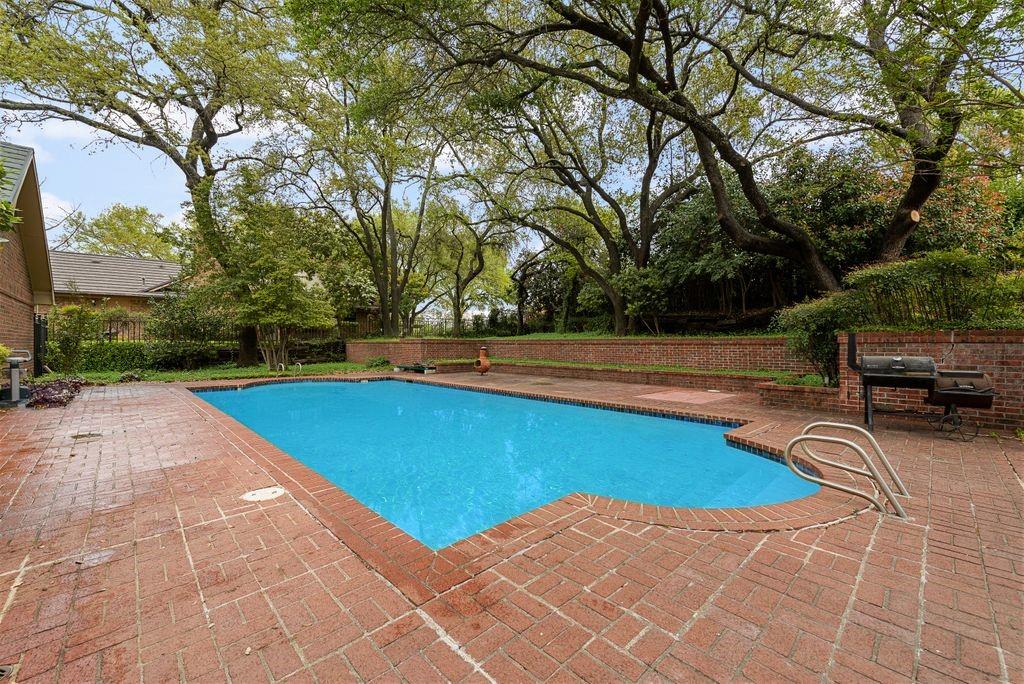 Rectangular swimming pool with integrated steps, surrounded by brick paver decking and a brick retaining wall