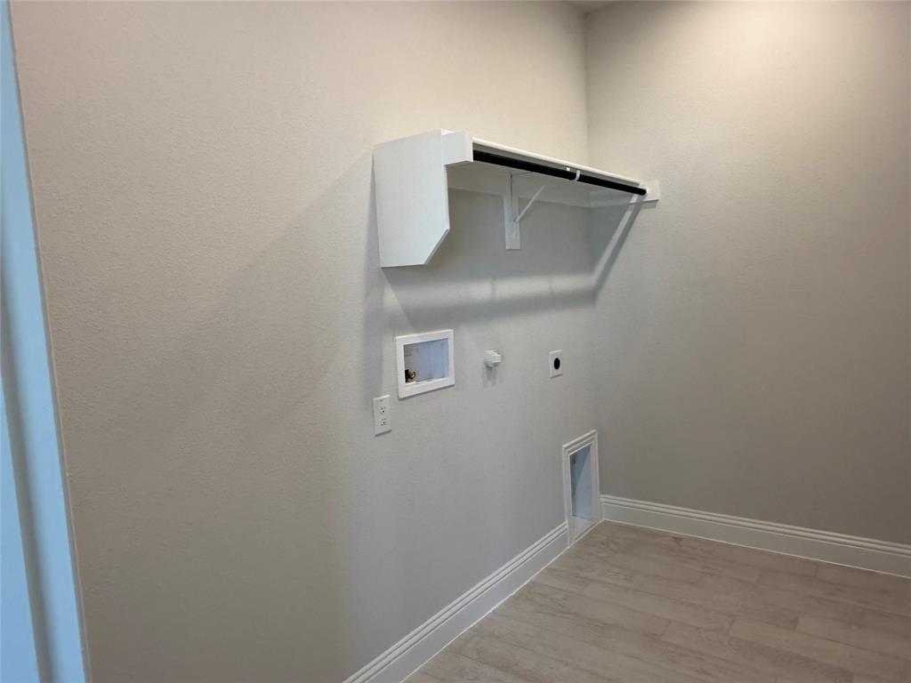 Utility room featuring a wall-mounted shelf with hanging rod, wood-finish flooring, and white baseboards