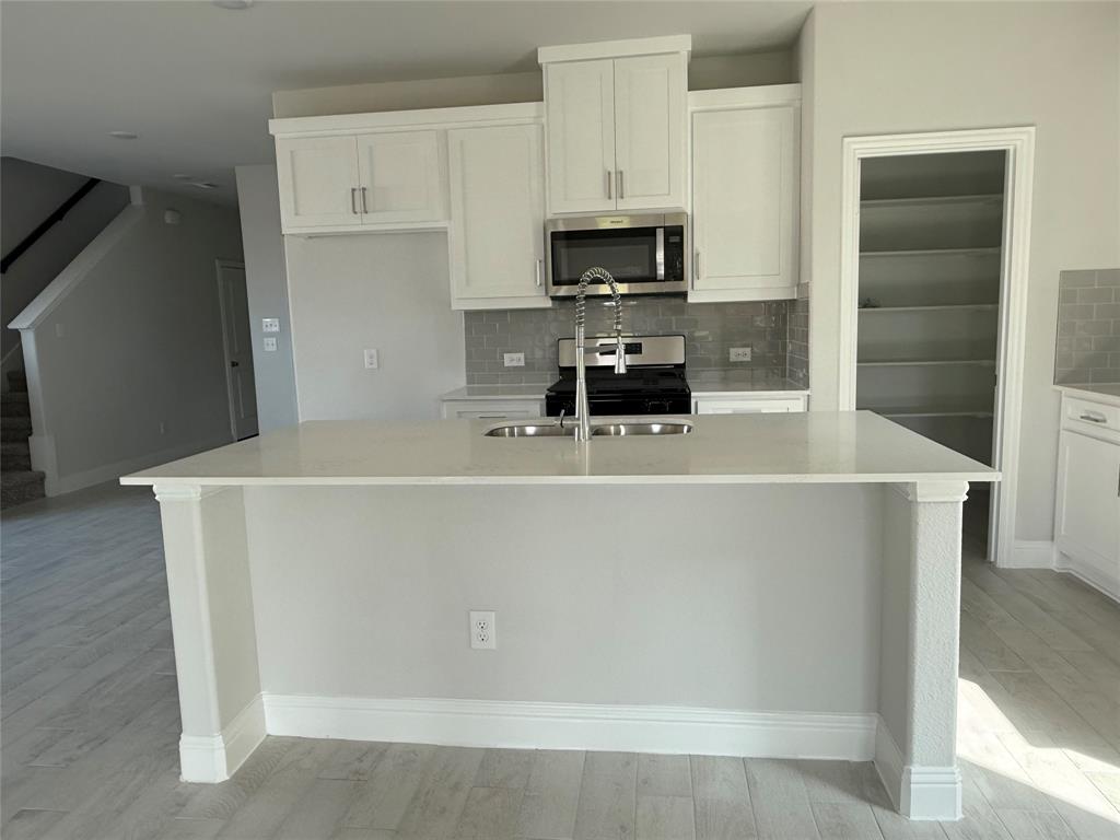 Kitchen featuring an island with an undermount sink, stainless steel appliances, light cabinetry, and a tile backsplash