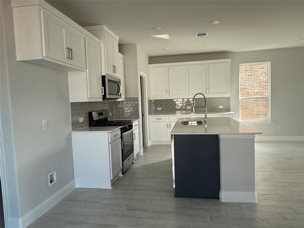 Modern kitchen featuring white cabinetry, stainless steel appliances, grey subway tile backsplash, a central island with a sink, and wood-finish flooring