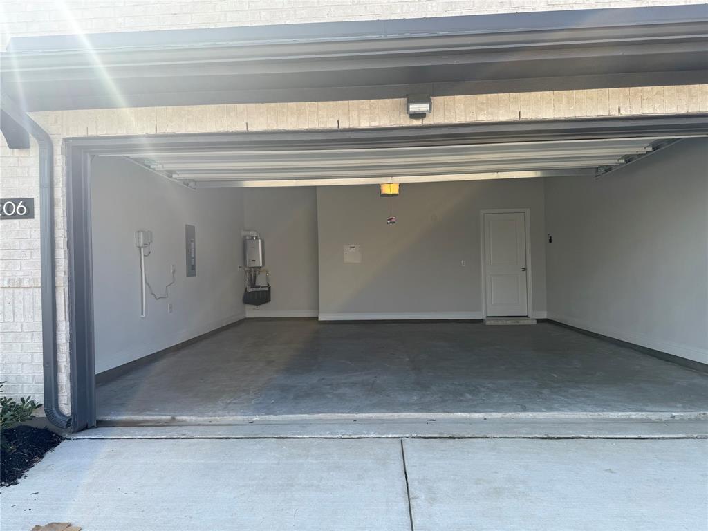 Spacious garage featuring concrete flooring, an interior access door, wall-mounted water heater, and overhead lighting Spacious garage featuring concrete flooring, an interior access door, wall-mounted water heater, and overhead lighting