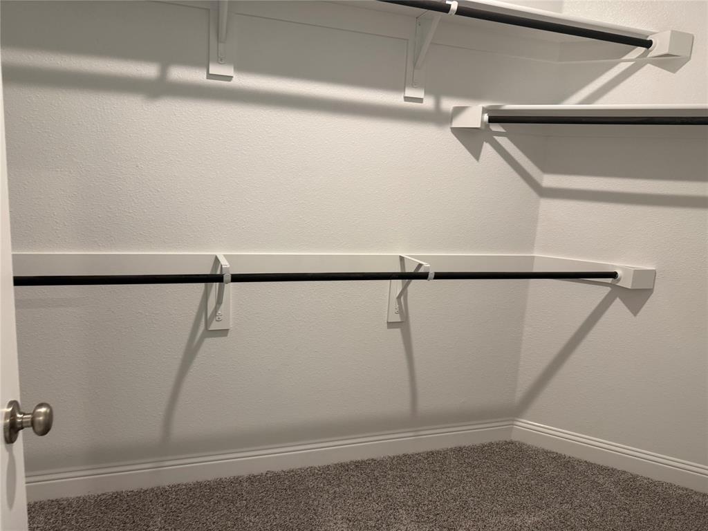 Built-in closet shelving system with multiple hanging rods, white wall finishes, and gray carpet flooring