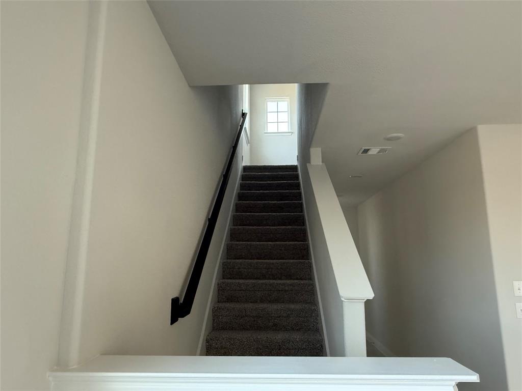 Carpeted staircase with a black handrail and white newel posts