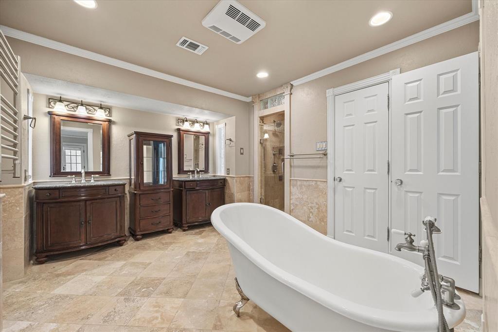 Update primary bath featuring a freestanding slipper tub, dual vanities, travertine flooring, and walk-in shower.  This spa-type retreat also features two closets on each side.