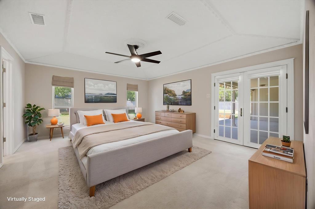 Virtually staged spacious primary bedroom featuring a tray ceiling, abundant natural light, and French doors leading to the patio.