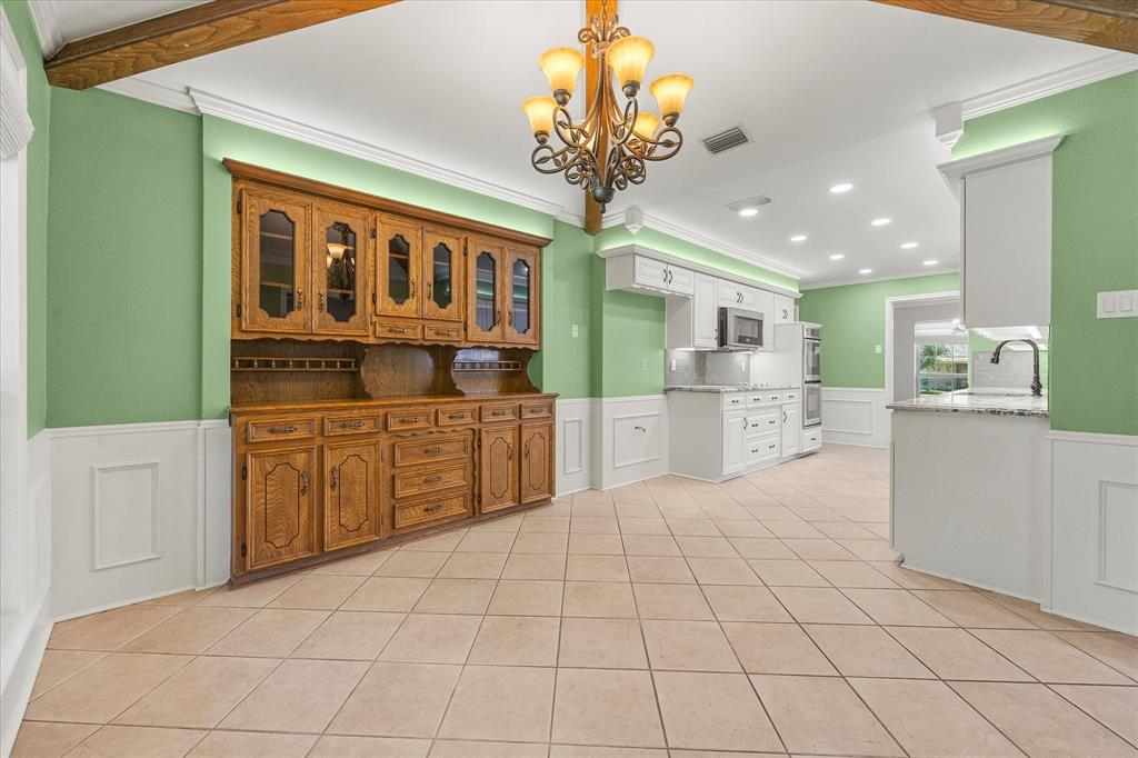 Breakfast and kitchen area featuring a built-in cabinet, decorative lighting, and neutral ceramic tile. While sitting at your breakfast table, you will have a view of the spacious backyard.