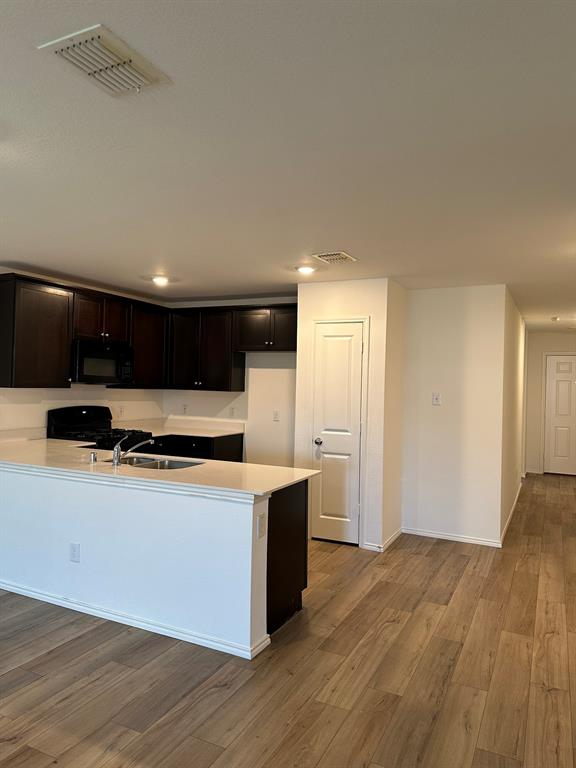 Kitchen with light wood-type flooring, black appliances, light countertops, a peninsula, and recessed lighting