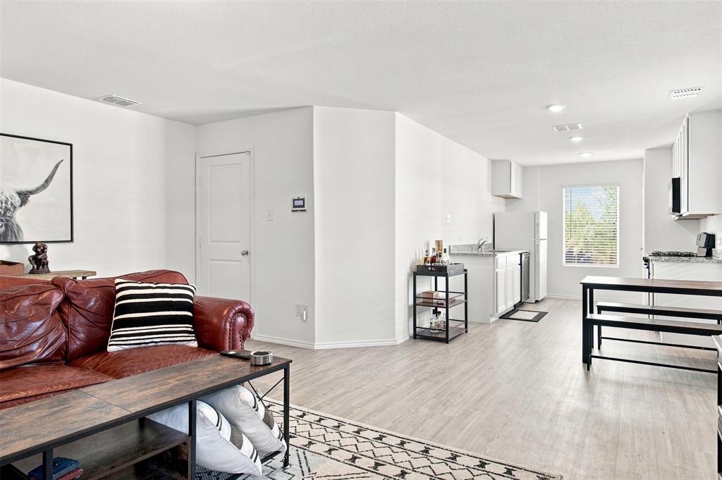 Open-concept living area featuring light wood-finish flooring, white walls, recessed lighting, and a kitchen with white cabinetry and granite countertops