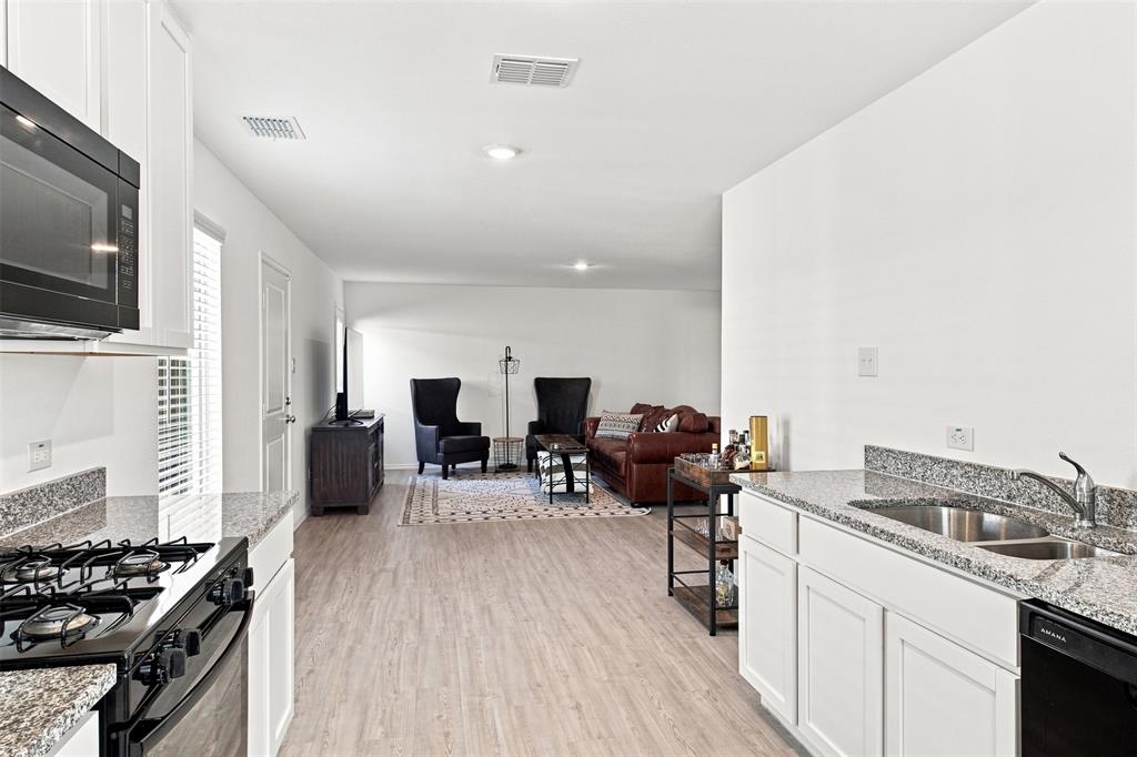 Kitchen featuring white cabinetry, granite countertops, a stainless steel sink, and a black built-in microwave