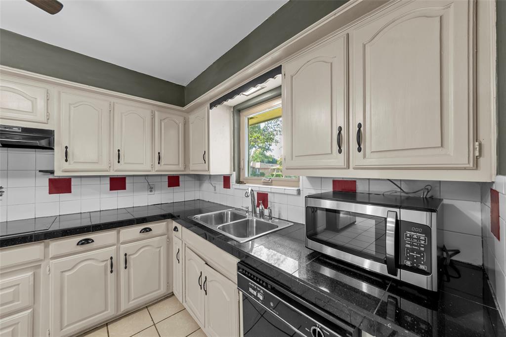 Cabinetry with arch panel doors, black countertop, dual basin stainless steel sink, and white tile backsplash with red accents