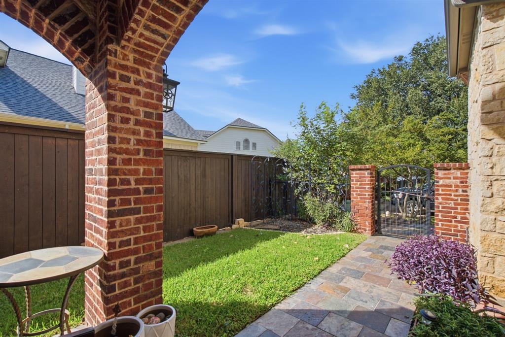 Covered front patio featuring a brick masonry archway, stone-tiled flooring, wood privacy fencing, and a decorative metal front gate.