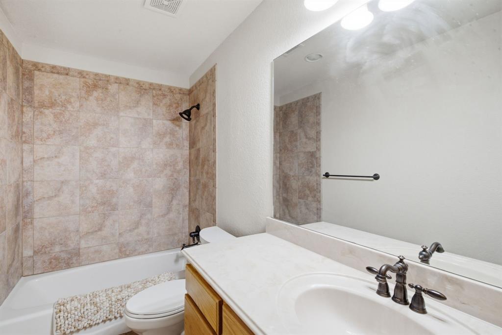 Upstairs bathroom featuring a neutral stone-tile tub surround, light-toned countertop with integrated basin, dark finish plumbing fixtures, large vanity mirror, and wood-finish cabinetry