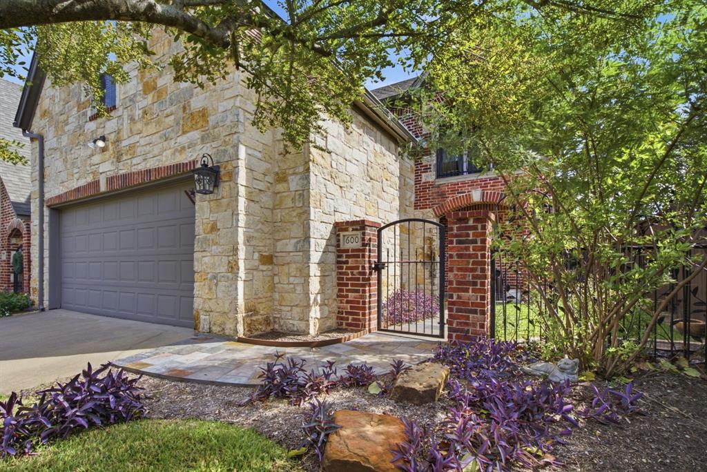 Exterior façade featuring natural stone masonry, red brick accents, an attached garage, and a gated masonry courtyard entry
