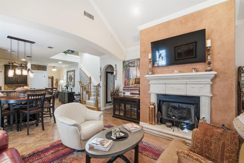 Vaulted ceiling featuring architectural crown molding, stone-finish gas fireplace surround with a detailed mantle, textured accent wall, and ceramic tile flooring