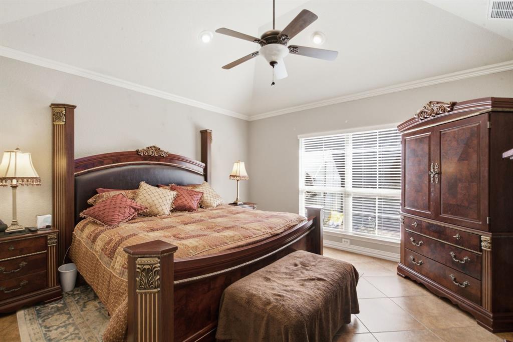 Primary bedroom with vaulted ceiling featuring a central multi-blade ceiling fan and neutral wall finish with crown molding, complemented by tile flooring and large windows with integrated blinds