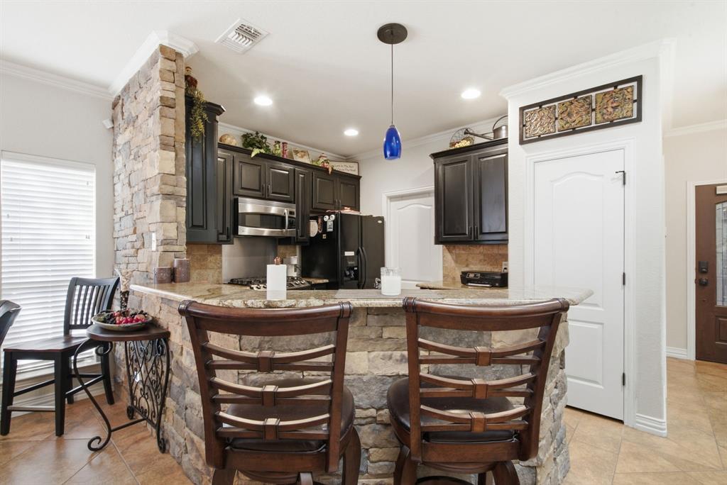 Kitchen featuring dark cabinetry, stone-veneer breakfast bar, natural stone countertop, tile backsplash, and recessed lighting