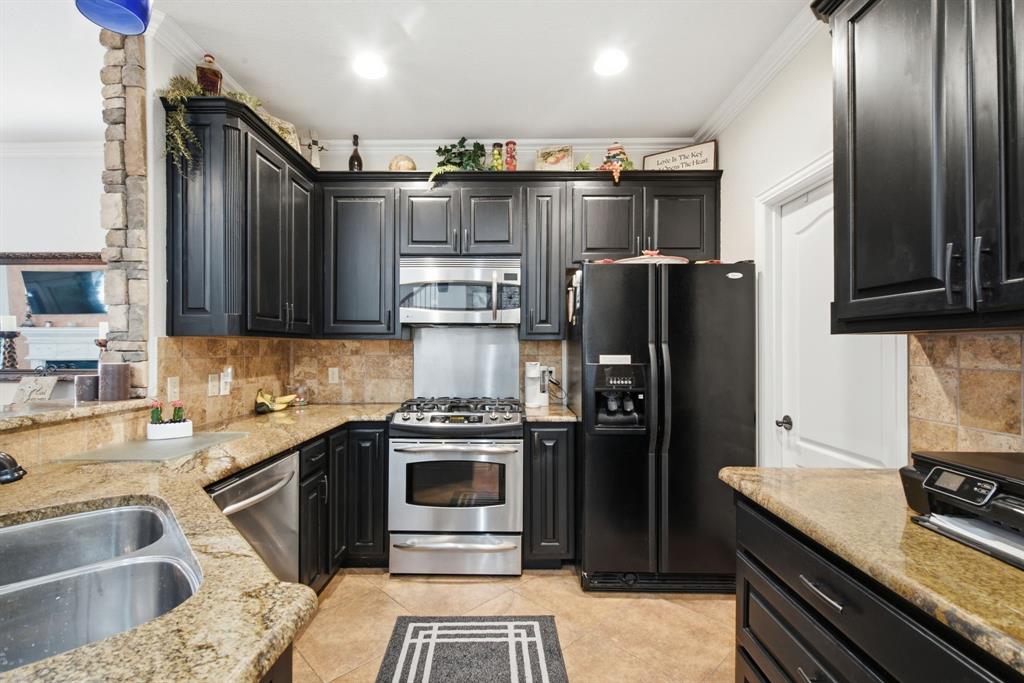 Kitchen featuring dark cabinetry, stone-finish countertops, tile backsplash, stainless steel appliances, and a stacked-stone pillar accent