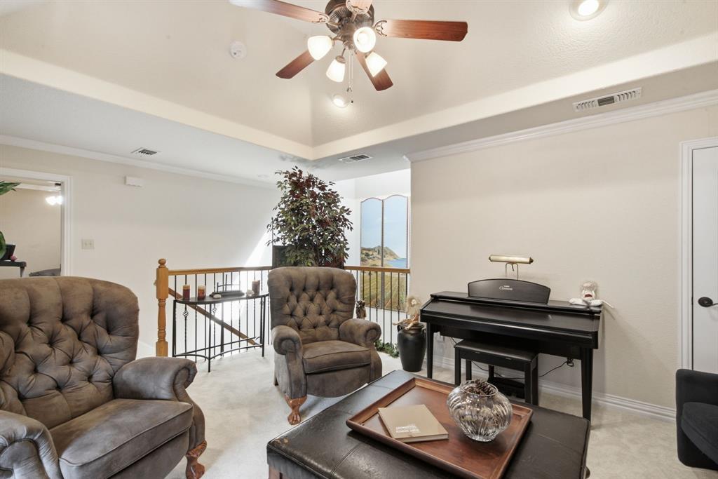 Upstairs living area with tray ceiling featuring recessed lighting and a central ceiling fan with multi-light fixture, offset by a decorative metal baluster railing