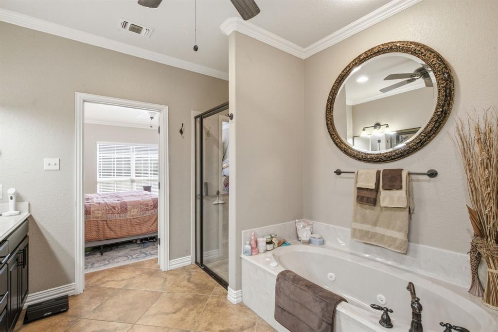 Jetted soaking tub with a stone-surround deck, glass-enclosed shower, dark-finish cabinetry, ornate circular wall mirror, and crown molding
