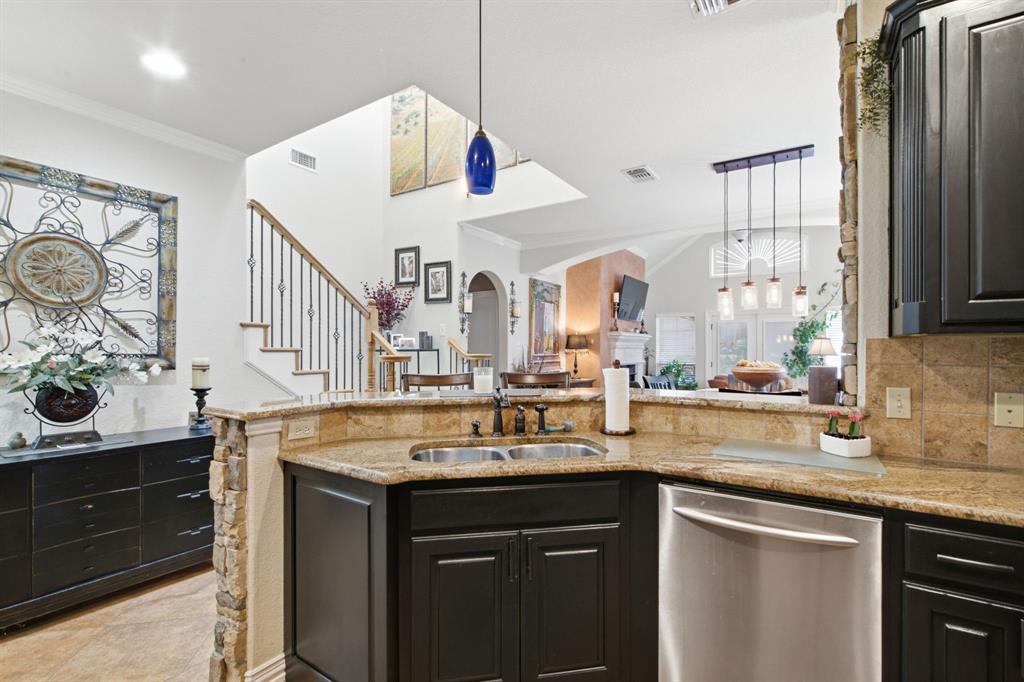 Kitchen featuring dark cabinetry, stone-surface countertops, tile backsplash, stainless steel dishwasher, and stacked-stone pillar detail