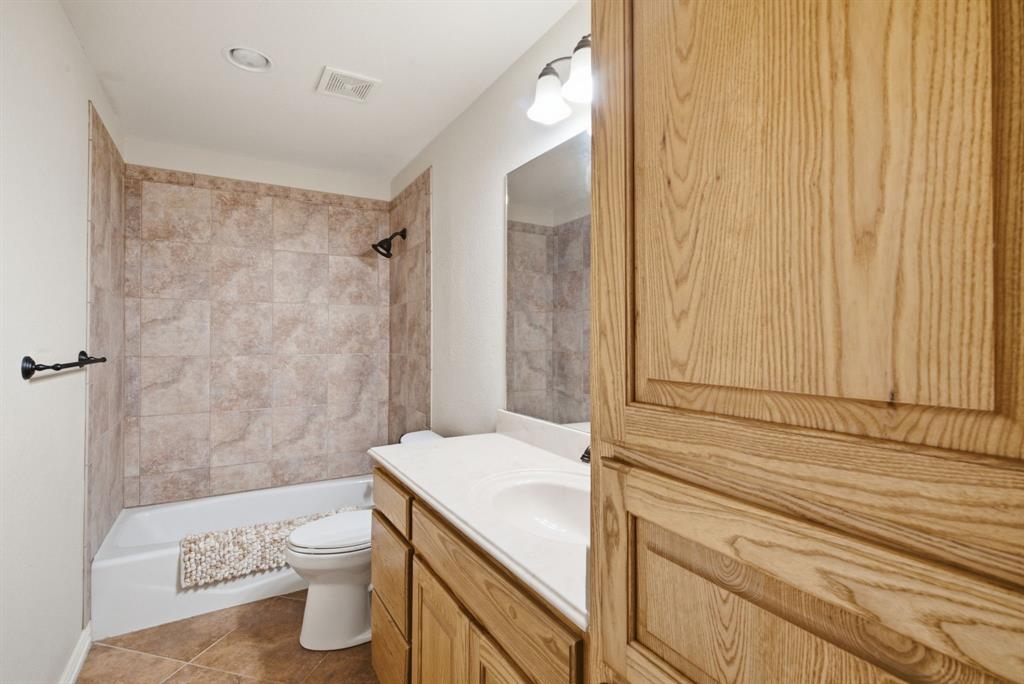 Upstairs bathroom featuring a vanity with wood-finish cabinetry, a white molded sink, a tiled tub-shower surround, and a wall-mounted mirror